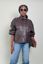 Woman wearing a brown leather jacket and sunglasses against a plain background