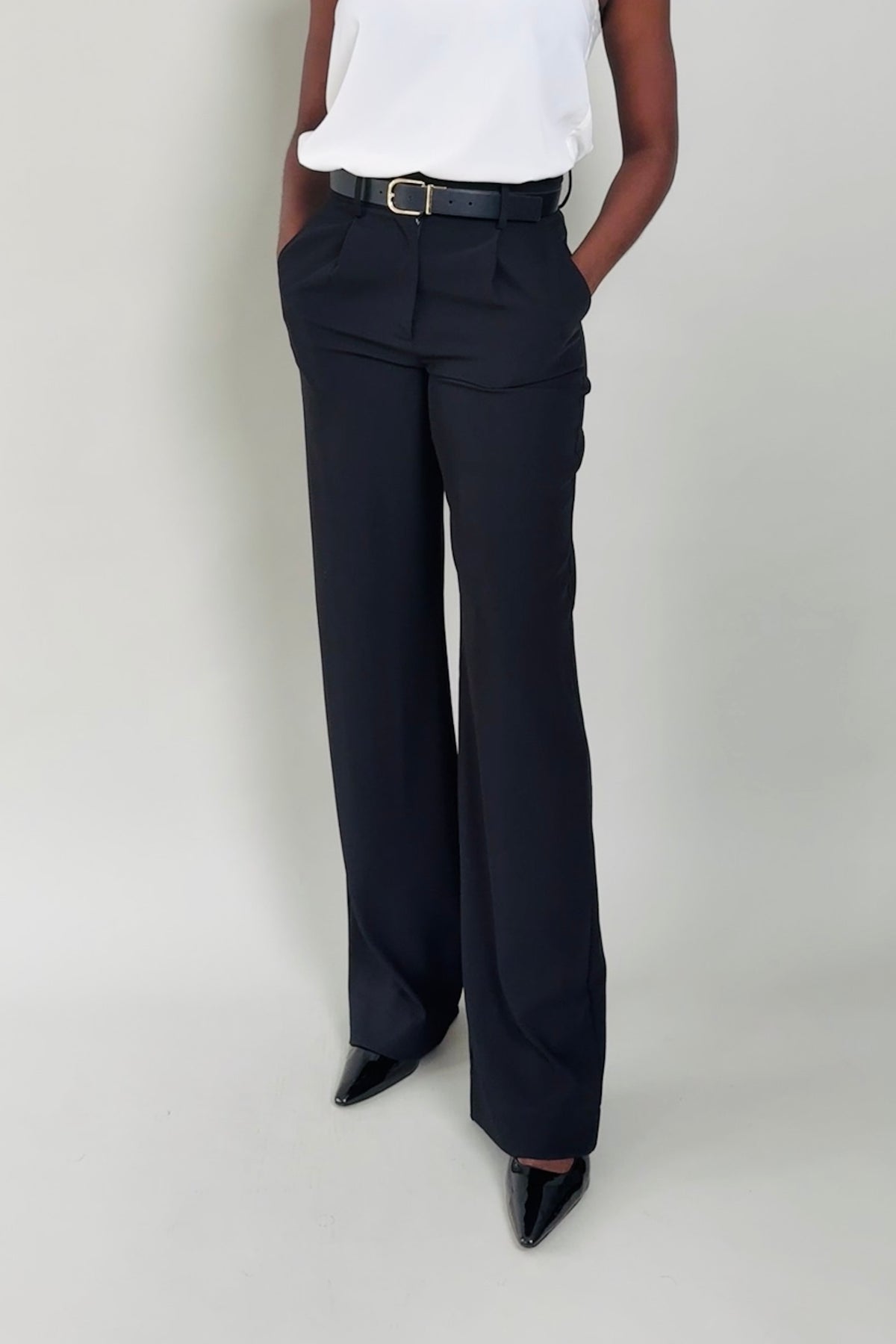 Person wearing black wide-leg pants and a white top on a plain background