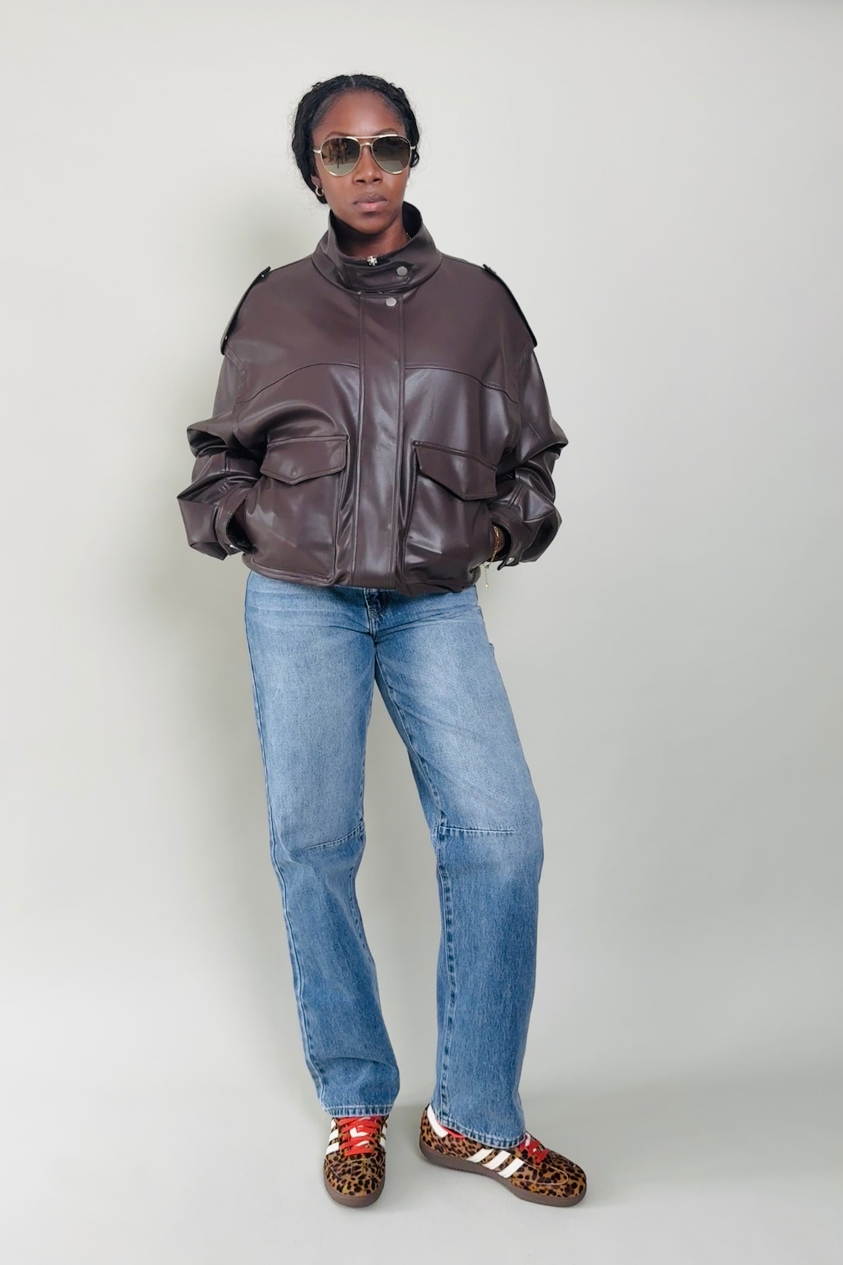 Woman wearing a brown leather jacket and blue jeans against a white background