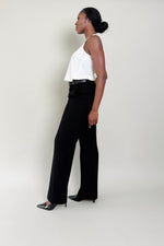 Woman wearing a white top and black pants against a plain background