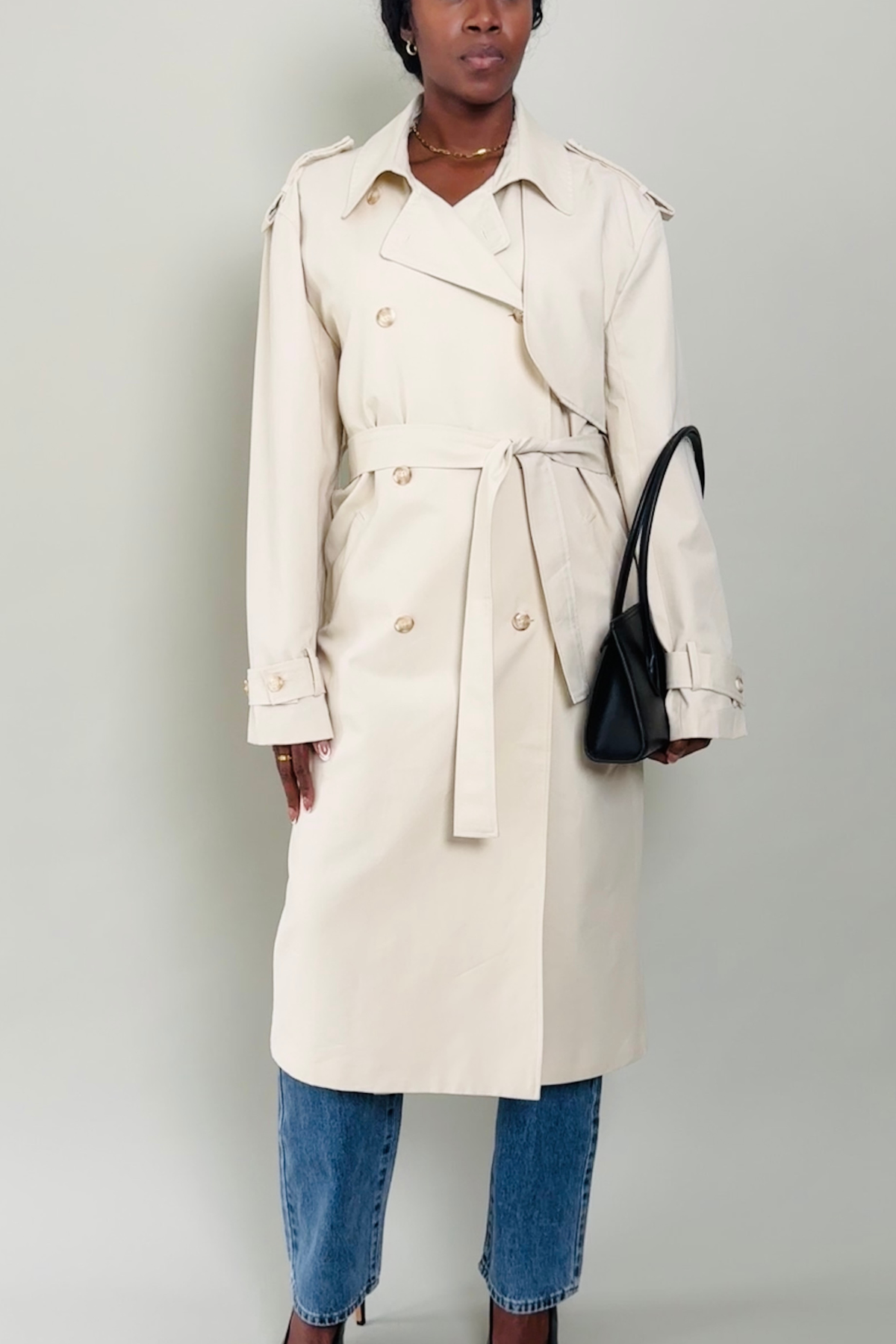Woman wearing a beige trench coat and blue jeans against a plain background